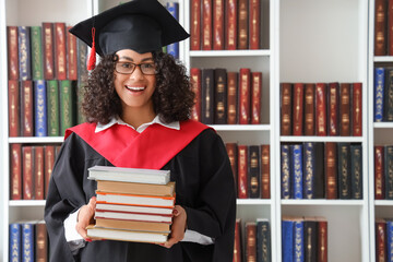 Happy African-American female graduate with books in library