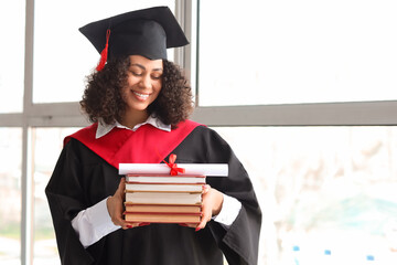Happy African-American female graduate with diploma and books near window