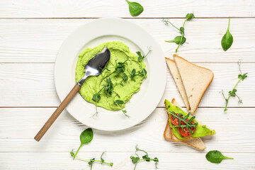 Composition with plate of tasty avocado hummus, fresh sprouts and bread on light wooden background