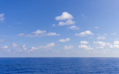 Clear Blue Sky Over Coastal Horizon with Scattered White Clouds
