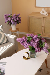 Vase with lilac flowers and alarm clock on table in living room