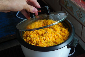 Hand lifting the lid of a rice cooker with yellow rice with tuna inside, typical Costa Rican food