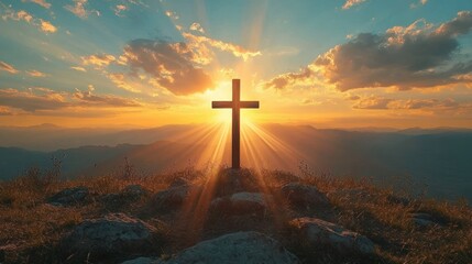 Wooden cross on rocky hilltop with sun rays shining through clouds during sunset over mountain landscape