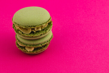 Green macarons stacked on a vibrant pink background