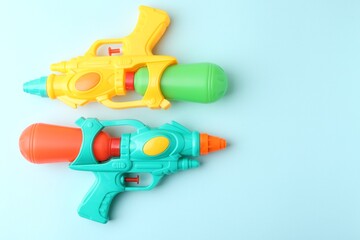 Bright plastic water guns on light blue background, top view. Space for text