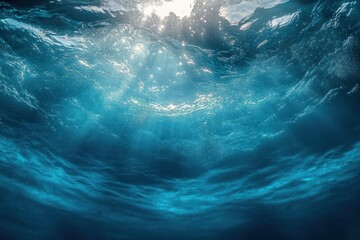 Underwater view looking up towards sunlight through clear, rippling ocean water with shimmering reflections and bubbles