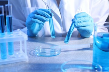Scientist with test tubes and Petri dish at table, closeup
