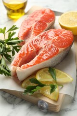 Seafood. Fresh raw salmon steaks, parsley and pieces of lemon on white marble table, closeup