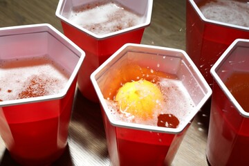 Plastic cups with drinks and ball on wooden table, closeup. Beer pong game
