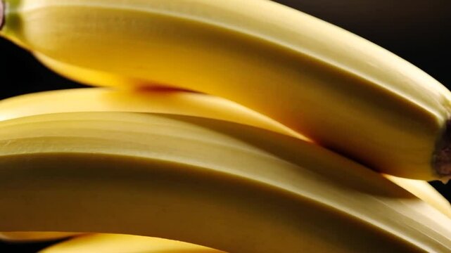 Close-up view of fresh yellow bananas arranged against a dark background. The image highlights the texture and color of the ripe fruit. The soft focus creates a visually appealing composition.