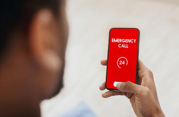 Emergency Call. View over shoulder of man holding phone with 24 hour support line on red screen...