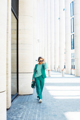 A stylish curly blonde woman walks along the streets of a summer city.