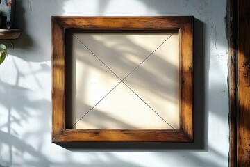 Empty wooden picture frame hanging on a white textured wall with window shadows casting patterns