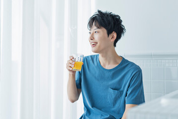 Fototapeta premium 朝にオレンジジュースを飲む若い男性