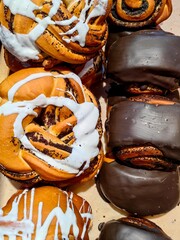 delicious baked goods are arranged on counter in bakery. assortment includes sweet rolls topped with icing and chocolate-covered pastries, enticing customers with their freshness. closeup.