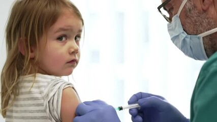 Doctor or nurse giving a vaccine to a child's arm while the child looks over his shoulder, brave child