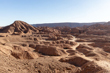 Undulating clay hills and dry canyons of the Cordillera de la Sal in the Atacama Desert, Chile, under clear sunlight. A raw and surreal natural landscape. Perfect for travel, editorial, and nature use