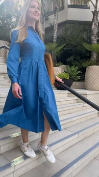 Vertical video of a young woman in a bright blue dress walking down white marble stairs on the street