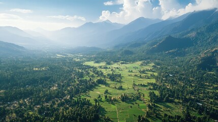 Fototapeta premium Aerial View of Lush Green Valley Surrounded by Majestic Mountains Under Bright Blue Sky and Soft White Clouds in Scenic Landscape