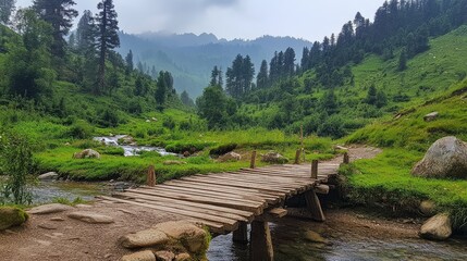 Wooden Bridge Over Serene Stream in Lush Green Mountain Valley Surrounded by Tall Trees and Foggy Mountains