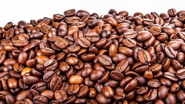 Brown coffee beans with shiny surface, scattered on a white background, highlighting the texture and color of the roasted beans