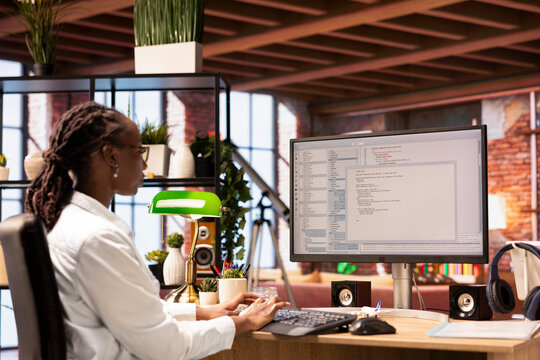 Woman in home office looking at UI on PC display, typing and executing programming code. Coding application UI used by IT developer writing and testing code in modern apartment