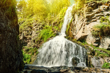 View of the seething stream of falling water of the Kamyshlinsky waterfall on a sunny summer day in the Altai Republic, Russia