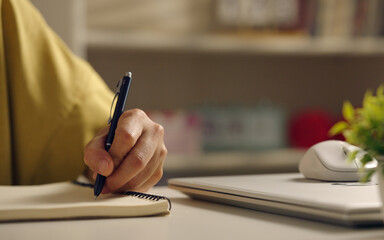 Asian woman works from home, surrounded by notes, a laptop, and messages. She browses the internet, writes ideas, and researches for her startup, utilizing wireless technology.