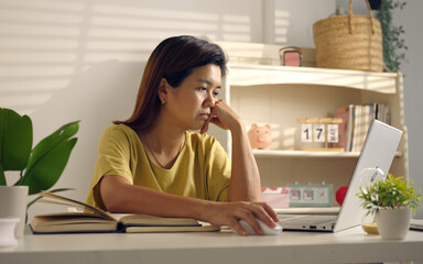 Asian woman works from home, surrounded by notes, a laptop, and messages. She browses the internet, writes ideas, and researches for her startup, utilizing wireless technology.