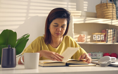 Asian woman works from home, surrounded by notes, a laptop, and messages. She browses the internet, writes ideas, and researches for her startup, utilizing wireless technology.