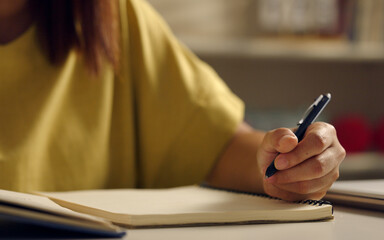 Asian woman works from home, surrounded by notes, a laptop, and messages. She browses the internet, writes ideas, and researches for her startup, utilizing wireless technology.