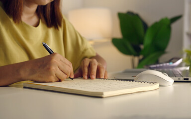 Asian woman works from home, surrounded by notes, a laptop, and messages. She browses the internet, writes ideas, and researches for her startup, utilizing wireless technology.