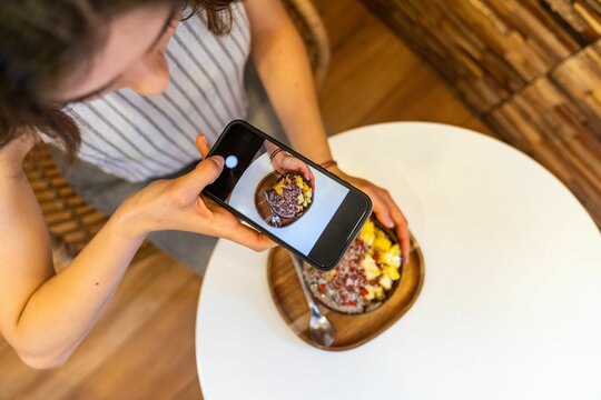 Woman taking photo of acai bowl with smartphone in cafe.