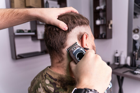 young man in a military uniform shaves his head bald for military service. A guy with a beard gets a haircut at a barber shop.