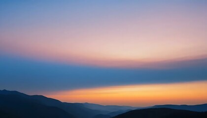Obraz premium Pastel hued sunset paints the layered silhouette of distant mountains with soft orange sunlight.