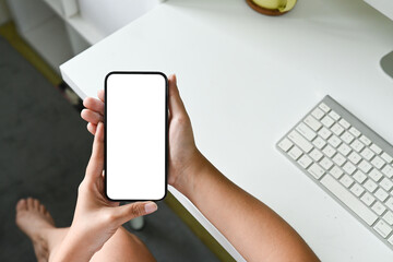 A person is holding a cell phone with a white screen. The phone is on a desk with a keyboard and a cup.