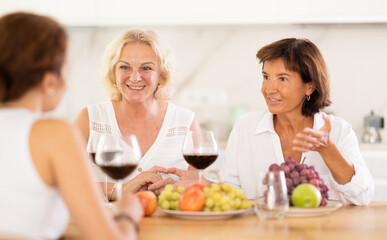 Girlfriends chatting and drinking wine at home party table in kitchen