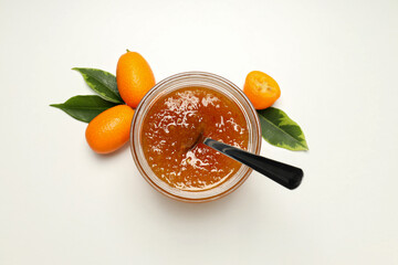 Fototapeta na wymiar Fresh kumquat fruits and jar of jam with spoon on white background, top view