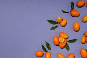 Whole and cut kumquat fruits and leaves on purple background, space for text