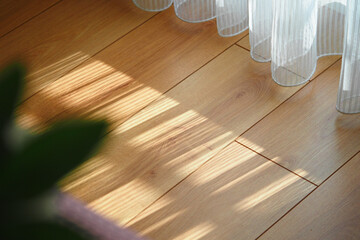 Soft sunlight casting shadows on wooden floor by a curtain