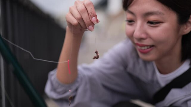 釣り針にイソメを付ける女性の釣り人のクローズアップ