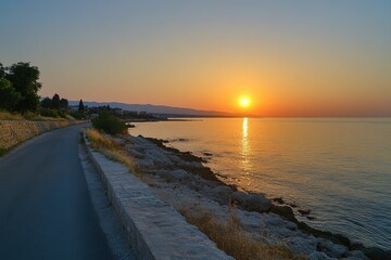 Coastal road at sunset, with calm sea and distant hills