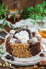 Chocolate biscuit cake with cream, nuts on wooden background with flowers and nuts. Holiday dessert, sweets and pastry, close up