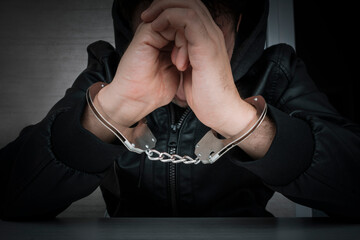 dangerous criminal is handcuffed in prison for interrogation. A repentant sad man with his head on...