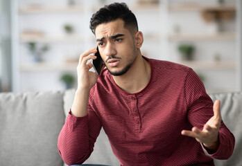 Closeup of sad arab guy sitting on couch, having conversation on mobile phone. Angry middle-eastern...
