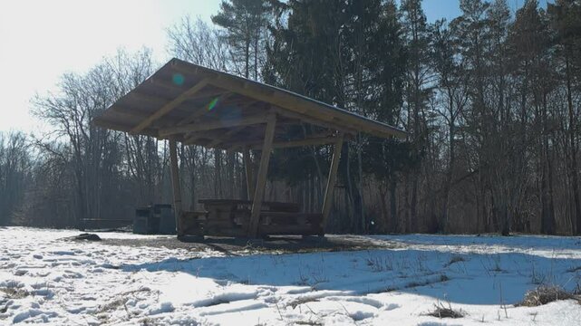Low perspective of a campfire site with wooden sheltered picnic table, serving as a rest stop in Tabasalu Nature Park on a sunny winter day. Snow covered landscape. Winter weekend get a away in nature