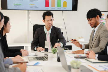 group of Asian businesspeople sit in a meeting in an office.