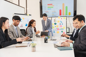 Asian business group discusses new project documents and presents in conference room, laughing and enjoying working together.