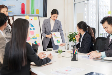 Group of Asian businesswomen presenting their work while their team listens to the explanation. They use laptops to check documents. They have tablets.
