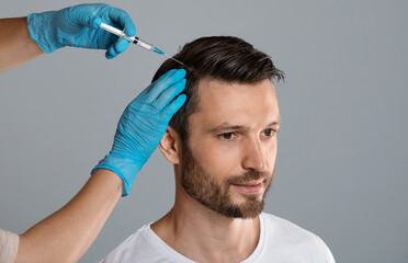 Mesotherapy for hair. Attractive man receiving injections in his head, grey studio background. Man...